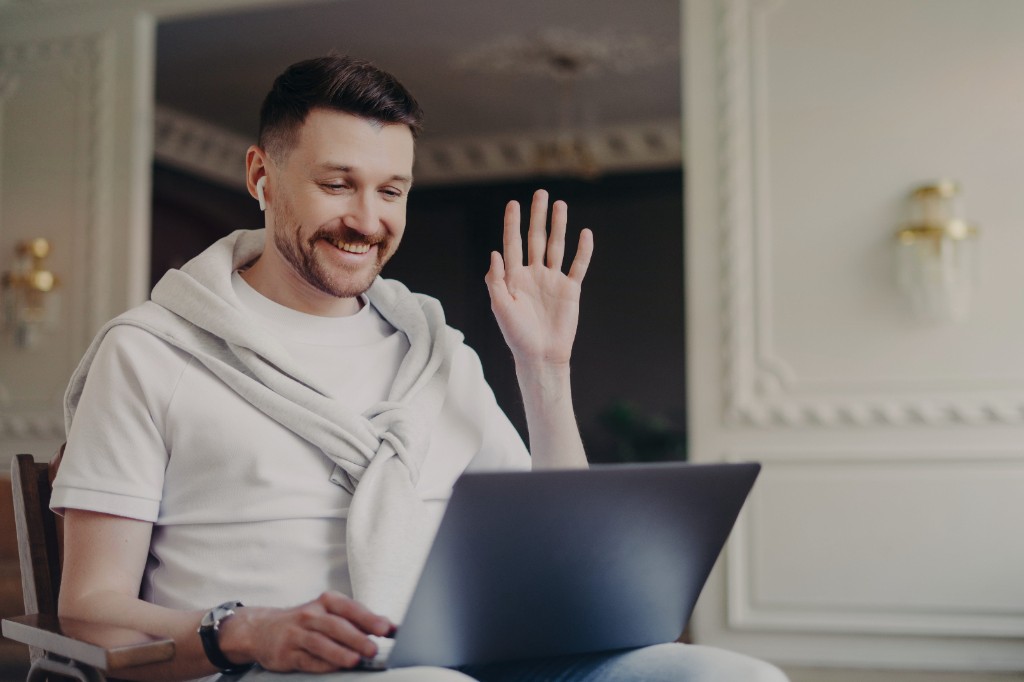 Person smiling and waving during a video call on a laptop at home